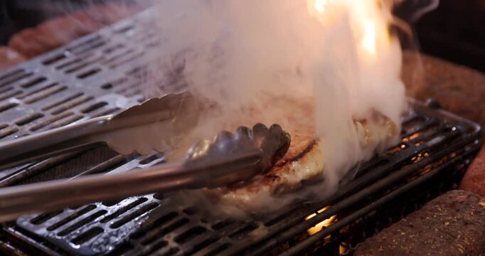 炭火の炎でこんがり焼き色がつく豚肉のアップ映像