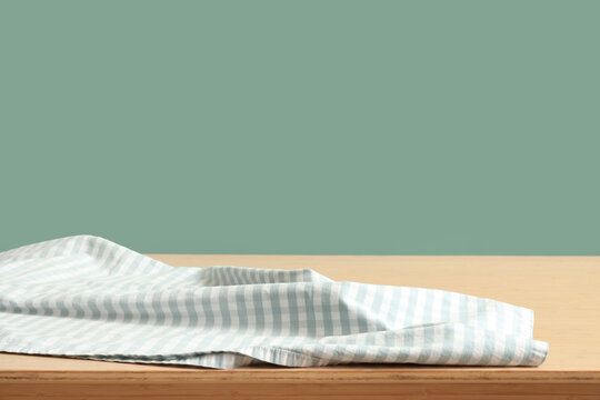 Empty wooden table with light blue gingham checkered fabric on green background for product display, the background is a solid green color, providing ample copy space for product display or text
