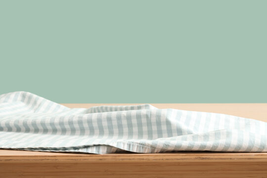 Empty wooden table with light blue gingham fabric on a soft green background for product display, the soft green background creates a gentle contrast