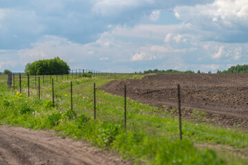 Obraz premium Rural plowed field beside dirt road under partly cloudy sky