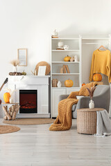Obraz premium Interior of living room with armchair, coffee table, autumn home decor on fireplace and pumpkins in shelving unit near white wall