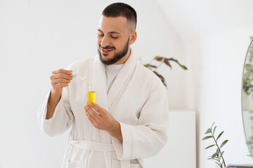 Fototapeta premium Handsome young man with bottle of vitamin E serum in bathroom