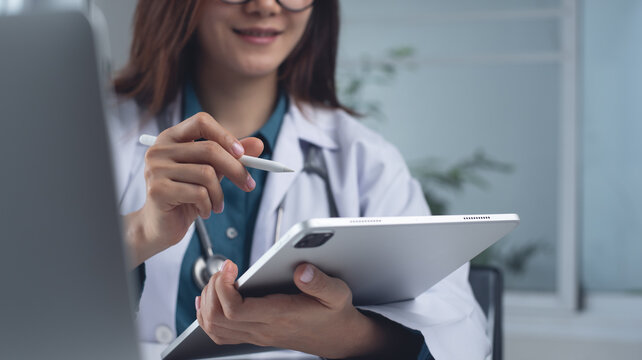 Female doctor using digital tablet at doctor's office. Doctor with stylus pen and tablet writing prescription, recording patient's health information