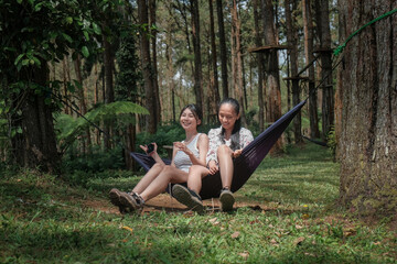 Obraz premium Asian Indonesian Female Friends Relaxing in Hammock During Forest Camping Trip