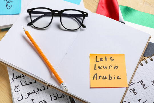 Arabic language learning with notebook, pencil, glasses, and "lets learn arabic" sticky note