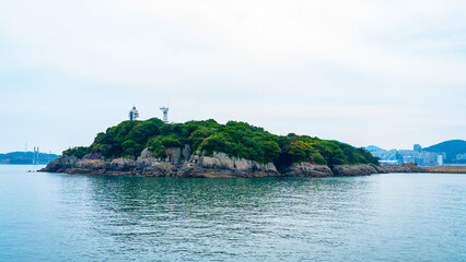 Obraz premium A small green island with a white lighthouse surrounded by blue sea in Yeosu