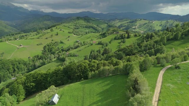 Spectacular fresh green pastures and rustic wooden barns in Simon under a moody stormy sky with beautiful sun rays, forward drone flight