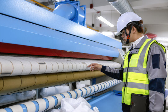 Factory engineer inspecting industrial flatwork ironer roller machinery, pointing at roller system and adjusting settings on large industrial pressing appliance checking ironing calender machine