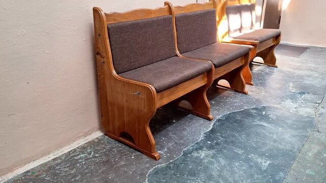 Row of sturdy wooden benches with cushioned seats and backrests against beige wall, natural light casting shadows, highlighting simple style and functional waiting area charm