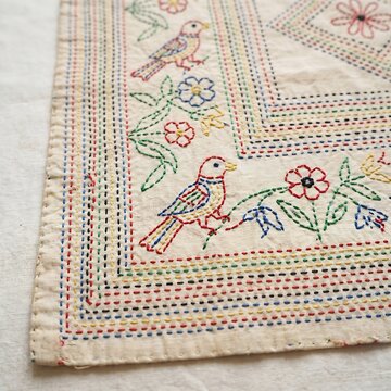 Traditional kantha embroidery with birds and flowers on cream fabric.