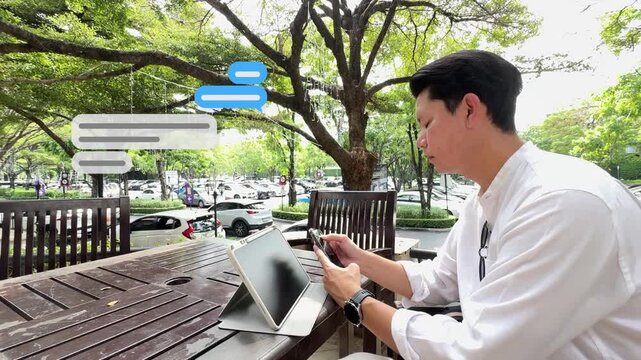 Side profile footage of a businessman sitting outdoors and typing text on his phone with green speech box graphics floating up.