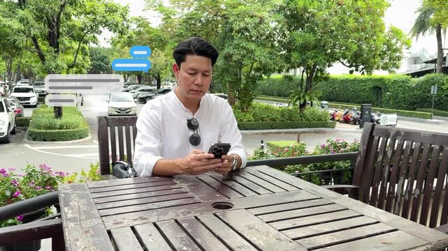 Wide shot of the businessman sitting at an outdoor garden table near the office, texting on his phone with rising chat box animations.