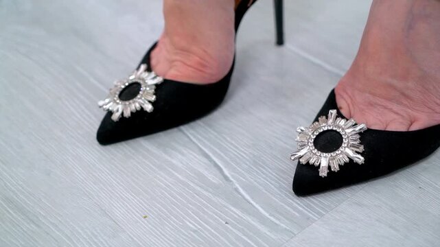 Elegant black velvet pointed-toe high heels with sparkling rhinestone sunburst embellishments, worn by a woman and photographed in close-up on a light textured floor. Sophisticated luxury footwear.