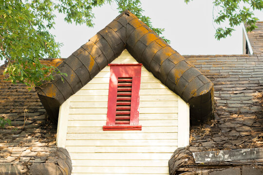 Moss-covered roof shingles surround a gable on a dilapidated house.