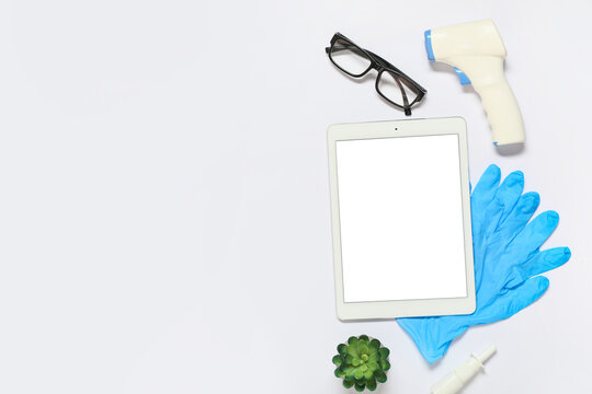 Medical healthcare technology flat lay with digital tablet, infrared thermometer, and protective gloves on white background