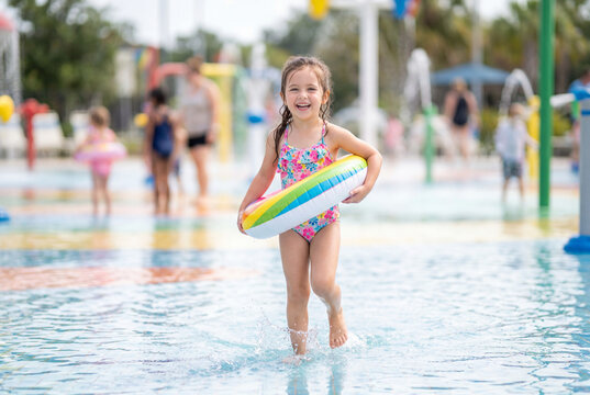 Happy young girl walking with an inflatable ring in a splash pad