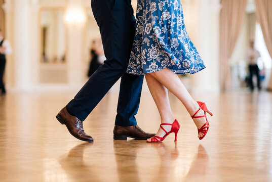 Lower half of a couple dancing gracefully in elegant attire on a polished ballroom floor