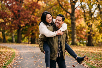 Fototapeta premium Happy young couple laughing playfully during a piggyback ride in a vibrant autumn park