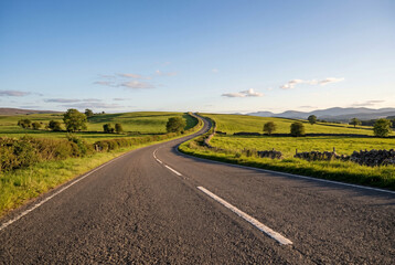 Naklejka premium Empty asphalt road winding through green grassy hills under clear sky