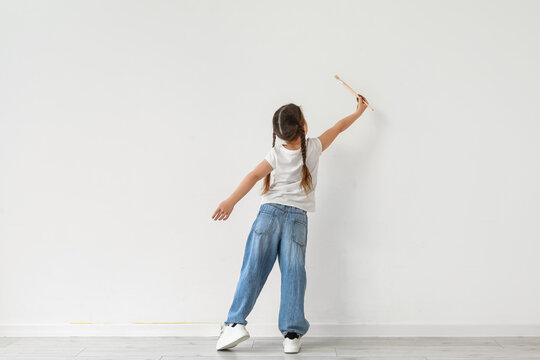 Young girl with braids painting on white wall, creative childhood development and artistic expression