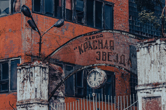 Rusty soviet factory gate with old clock and cyrillic sign