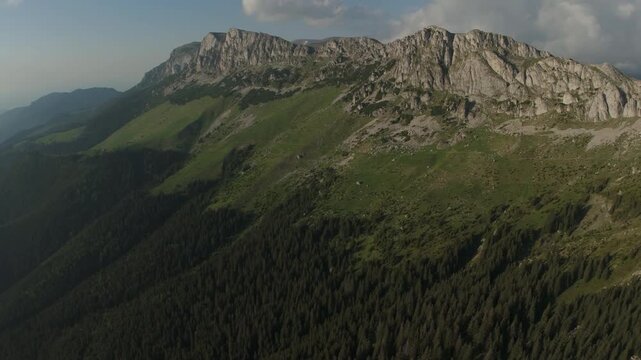 Breathtaking wide panorama of the Bucegi Mountains western ridge and massive limestone peaks during a serene golden hour, high altitude aerial pan right, graded