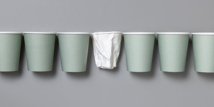Creative arrangement of light green disposable cups with one crumpled white paper cup in between