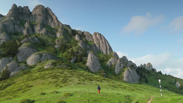 Triumphant lone hiker raising arms victoriously and walking out of static frame with conglomerate rock formations in the Ciucas Mountains, Romania, perfect copy space on clear sky