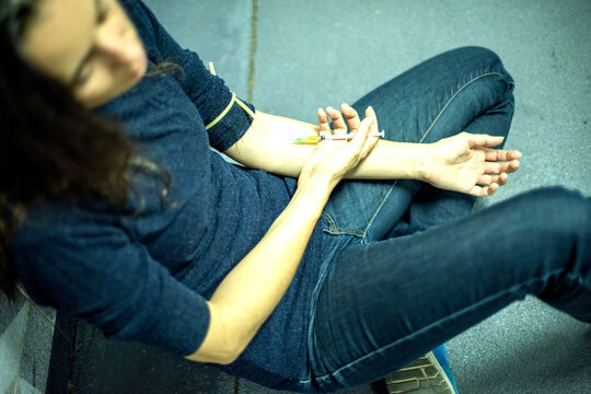 Person sitting on the floor, preparing to inject with a syringe.