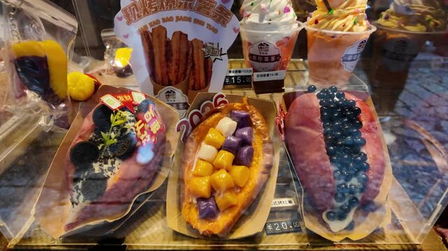 Wangxian Valley, China, 04 April 2026 ? A Chinese street food stall displays decorated baked sweet potatoes with colorful toppings and ice cream cups behind a clear acrylic case.