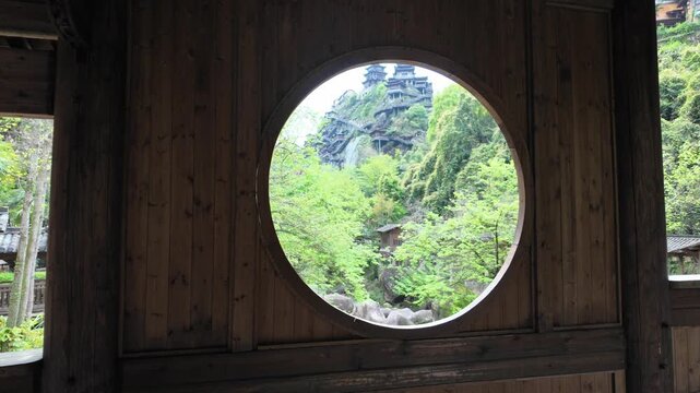 Wangxian Valley, China, 04 April 2026 ? Round moon gate window frames cliffside pagodas above a rocky river gorge surrounded by lush spring foliage in Wangxian Valley.