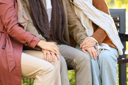 Man with two women sitting on bench in autumn park, closeup. Polyamory concept