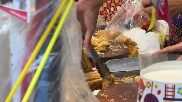 4K shot of a street vendor pouring out and chopping crispy deep-fried vegetarian tofu and taro snacks for customers on a round cutting board.