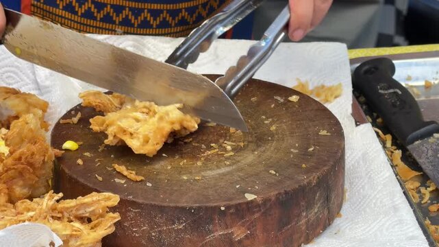 Close-up 4K video of sharp knife slicing through crispy deep-fried golden tofu and taro blocks on a round wooden cutting board.