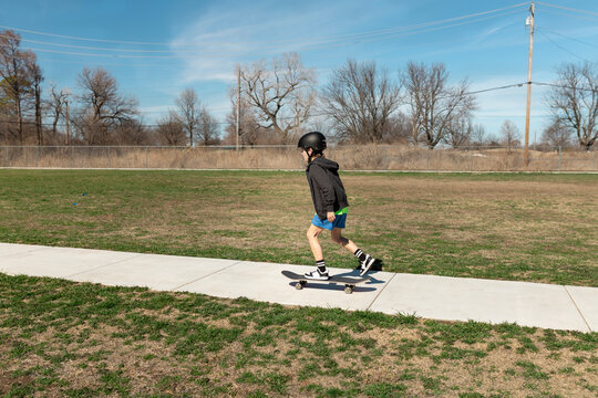 Boy pushing a skateboard along a sidewalk