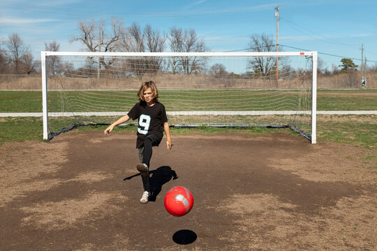 Young boy practices kicking a red soccer ball