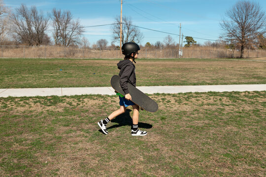Young boy with helmet carries his skateboard