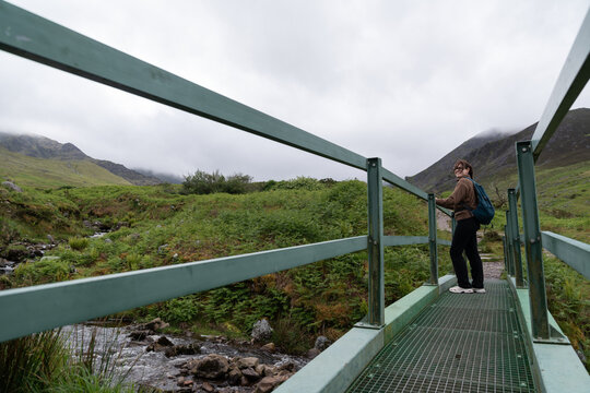 Woman hiking mountain trail crossing metal bridge