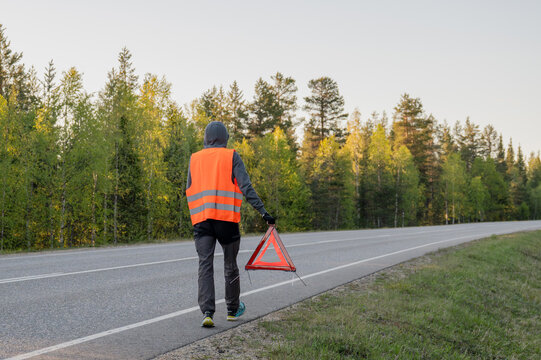 Man in safety vest with warning triangle on road