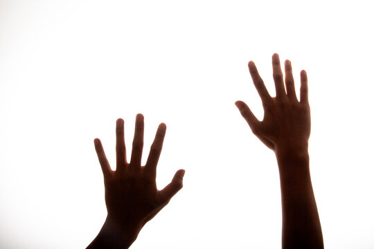 Silhouette of two hands reaching up against a bright white background