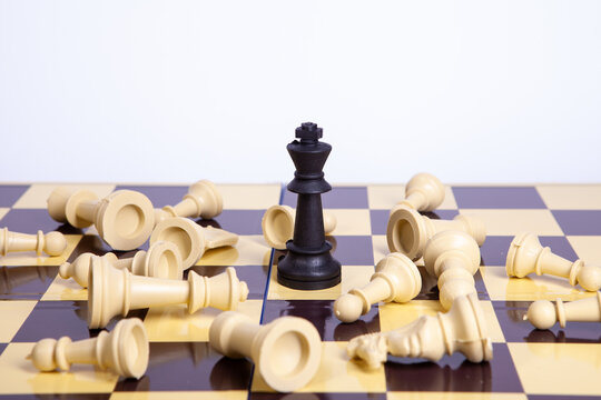 Black chess king piece standing alone among fallen white pieces on chessboard