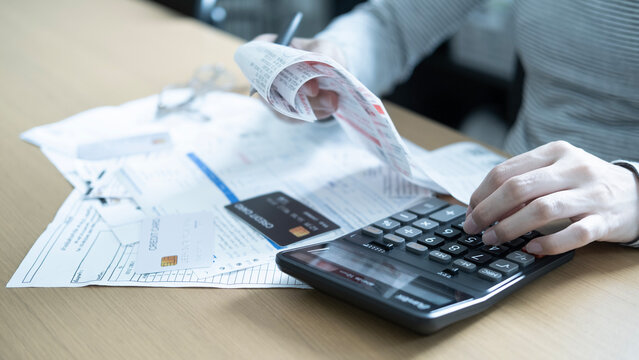 Person calculating monthly household bills with receipts, invoices, credit cards and a calculator for debt management and family expense planning.