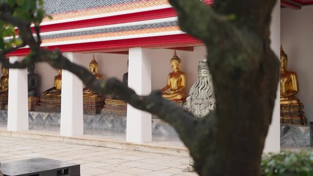 Pull Out &ndash; Camera Movement in Wat Pho temple in Pull-out shot in Wat Pho, Bangkok, showcasing a row of golden Buddha statues and a stone Chinese guardian, embodying the spiritual heritage and historic