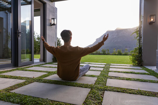 Stone pavers are sitting in grass strips on modern patio with pergola casting soft shadows