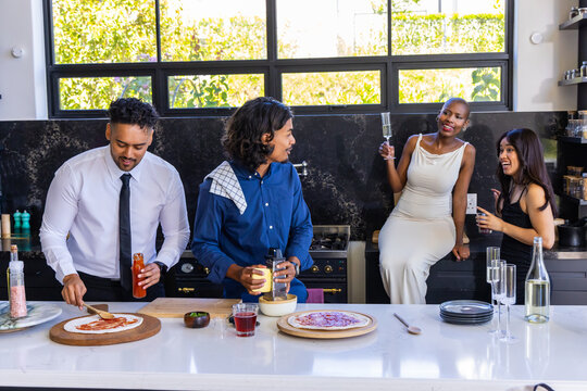 African American friends meeting at kitchen island making pizzas with pizza boards, wearing shirts