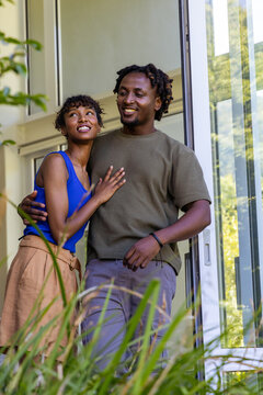African American couple standing in doorway, leaning together near sliding glass door with plants