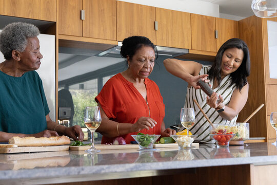 African American multigenerational family slicing baguette and tossing salad at kitchen island