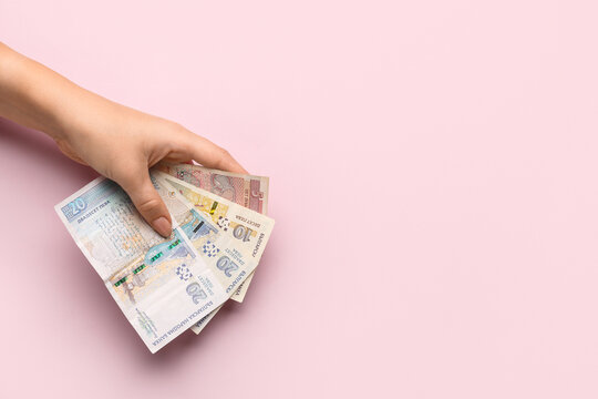 Female hand holding Bulgarian lev banknotes on pink background