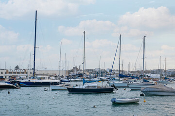 Obraz premium Sailboats and yachts moored in a bustling harbor with coastal cityscape and cloudy sky, numerous sailboats and yachts are moored in a busy harbor, reflecting a vibrant maritime scene