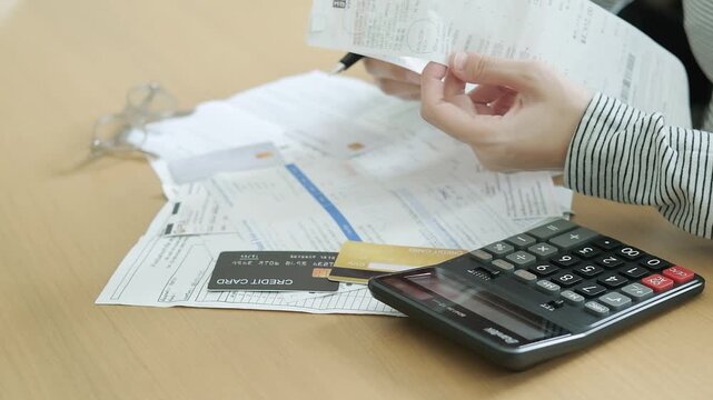 Hands checking long receipts with a calculator, credit card and financial documents for household expense tracking and monthly debt planning.
